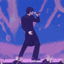 a man in a black coat is singing into a microphone while standing on a stage in front of a crowd .