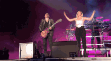 a man playing a guitar stands next to a woman on a stage