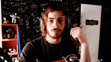a man with a beard wearing headphones is standing in front of a blackboard with graffiti on it .