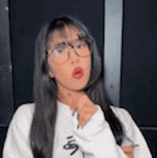a young woman wearing glasses and a white sweater is making a funny face .
