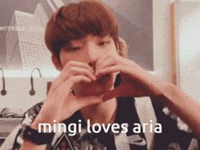 a young man making a heart shape with his hands and the words mingi loves aria