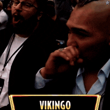 a man covering his mouth in front of a vikingo sign