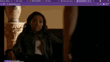 a woman in a leather jacket sits on a couch in a room