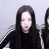 a girl with long black hair is wearing a black jacket with white stripes