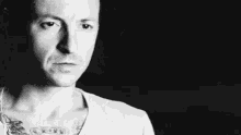 a close up of a man 's face with a tattoo on his chest in a black and white photo .