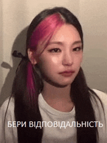 a woman with pink hair is wearing a white t-shirt and making a sad face .