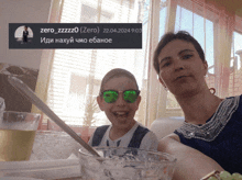 a girl wearing green sunglasses sits next to a woman in front of a sign that says zero_zzzz0