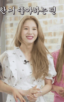 a woman in a white dress is smiling in front of a brick wall with korean writing on it