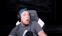 a man is sitting in a gaming chair wearing headphones and a hat .