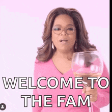 a woman in a pink shirt is holding a glass of wine with the words welcome to the fam below her