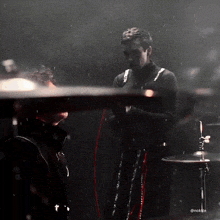 a man in a black turtleneck stands in front of a drum set with the hashtag @noktee on the bottom