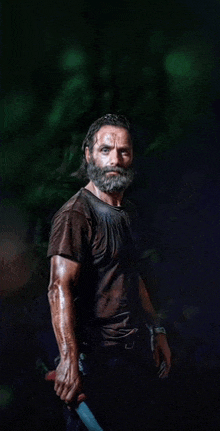 a man with a beard is holding a knife in his hand in a dark room .