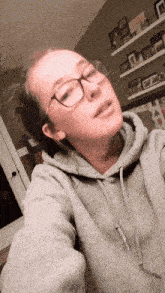 a woman wearing glasses and a grey hoodie looks at the camera