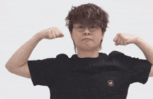 a man wearing glasses and a black shirt flexes his arms