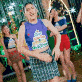 a woman wearing a purple crop top and a green plaid skirt is dancing in front of a group of women .