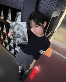 a girl in a black sweater and grey skirt holds a book