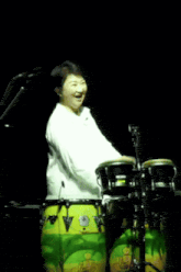 a woman in a white shirt is smiling while playing a drum set