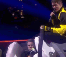 a man in a yellow jacket is holding a microphone