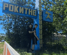 two people standing in front of a blue sign that says rokithe