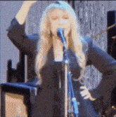 a woman is singing into a microphone with her hand in the air
