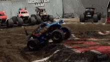a monster jam sign is behind some monster trucks on a dirt track