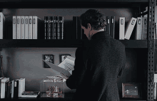 a man is reading a book in front of a shelf with binders that have the letter o on it