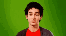 a young man wearing a red shirt and a black cardigan is making a funny face .
