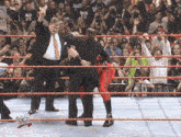 a man in a suit and tie stands in a wrestling ring with a crowd behind him