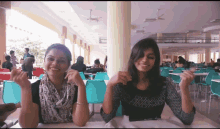 two girls are sitting at a table in a cafeteria