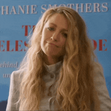 a woman with long blonde hair stands in front of a sign that says hanie smothers