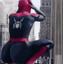 a man in a spiderman costume is squatting down in front of a building in a city .