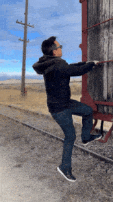 a man in a black jacket is standing on train tracks pulling something