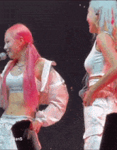 two women with pink hair are standing on a stage .