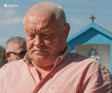 a man in a pink and white striped shirt is standing in front of a blue building with a cross on it .