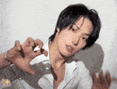 a young man wearing a white shirt and a necklace is making a cat face with his hands .