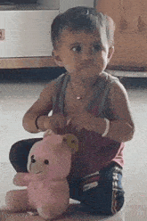 a baby is sitting on the floor with a pink teddy bear .