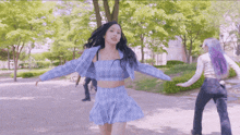 a woman in a blue plaid top and skirt dancing in a park