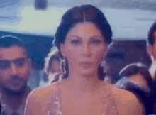 a woman in a dress is standing in front of a crowd of people and looking at the camera .