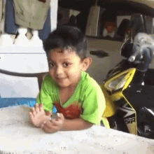 a young boy in a green shirt is sitting at a table next to a motorcycle .