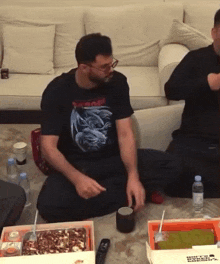 a man wearing a black shirt with a dragon on it sits on the floor next to a box of food