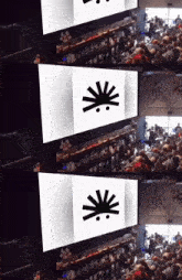 a group of people are sitting in front of a large screen with a black sun on it