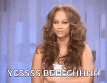 a woman with long hair is sitting in a chair with her hands folded and says yesss beeechhhh .