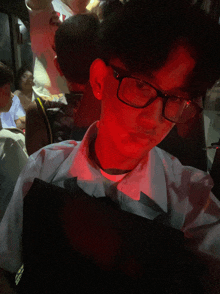 a man wearing glasses is sitting in a dark room with a red light behind him