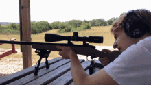 a man wearing ear muffs is aiming a rifle with a scope