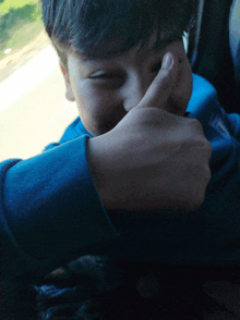 a young boy in a blue shirt covering his face with his hand