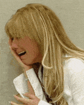 a woman with long blonde hair is laughing with her hand to her face