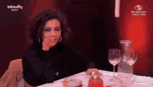 a woman is sitting at a table with wine glasses and a bottle of wine .