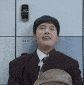 a young man in a suit and tie is sitting in a locker room holding a hat and smiling .