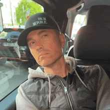 a man sitting in a car wearing a hat that says palm republic