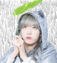 a girl wearing a hooded jacket holds a green leaf in her hands